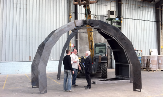 Photographie représentant trois personnes discutant devant une structure métallique en cours de construction de la forme d’une structure d’igloo