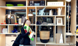 Photographie montrant des objets de tous types en libre-service, disponibles sur des étagères, et une cliente de l’hôtel partant avec un coussin qu'elle vient de prendre dans cette bibliothèque d'objets